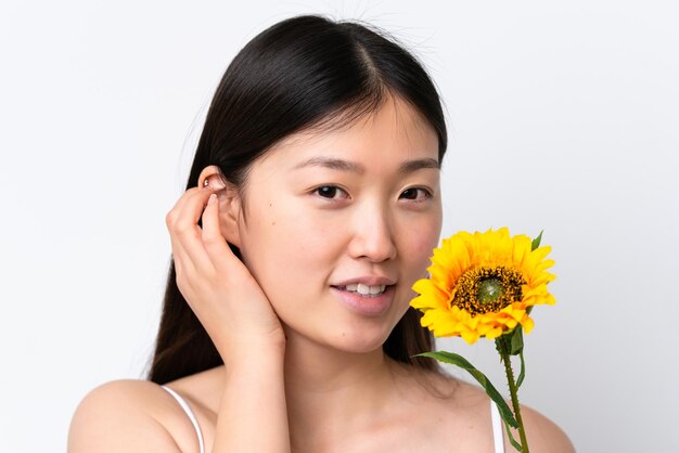 Young Chinese woman isolated on white background holding a sunflower while smiling Close up portrait