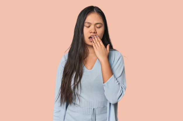Молодая китайская женщина изолирована зевает, показывая усталый жест, покрывающий рот рукой.