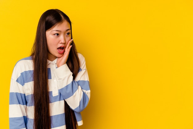 Young chinese woman isolated on yellow background being shocked because of something she has seen