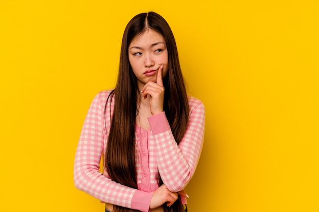 Young chinese woman isolated on yellow background contemplating, planning a strategy, thinking about the way of a business