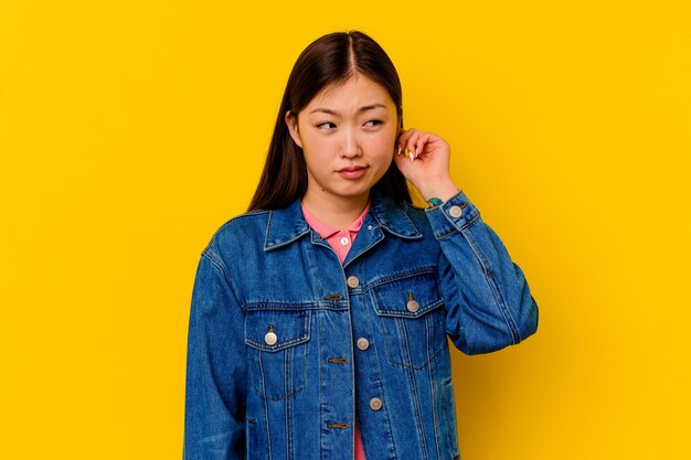 Young chinese woman isolated on yellow background covering ears with fingers, stressed and desperate by a loudly ambient.