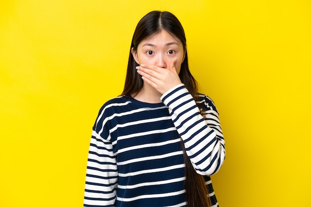 手で口を覆っている黄色の背景に分離された若い中国人女性
