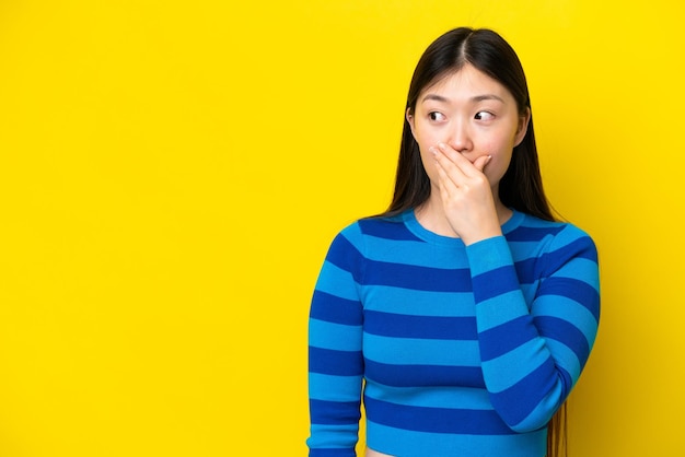 Young chinese woman isolated on yellow background doing surprise gesture while looking to the side