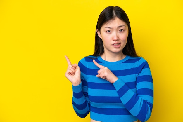 Young Chinese woman isolated on yellow background frightened and pointing to the side