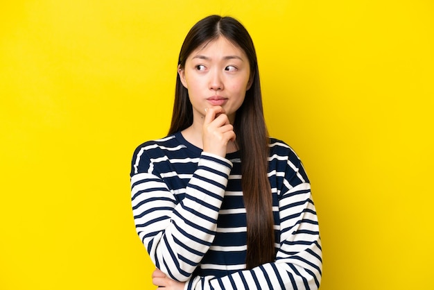 Young chinese woman isolated on yellow background having doubts and thinking