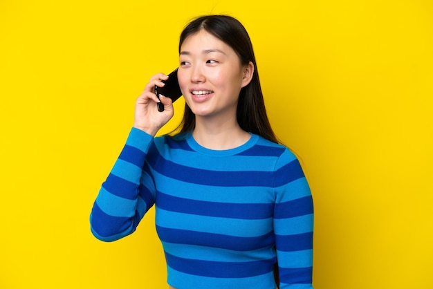 Young Chinese woman isolated on yellow background keeping a conversation with the mobile phone