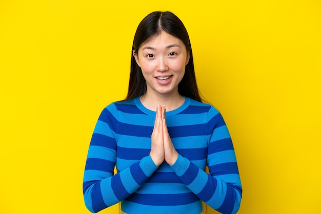 노란색 배경에 격리된 젊은 중국 여성이 손바닥을 함께 유지합니다.