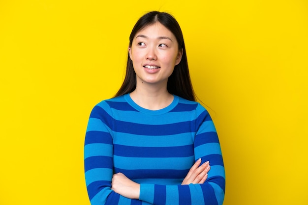 Young Chinese woman isolated on yellow background looking up while smiling