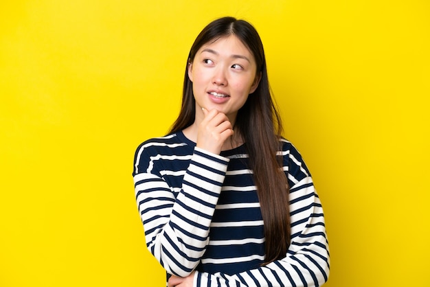 Young Chinese woman isolated on yellow background and looking up