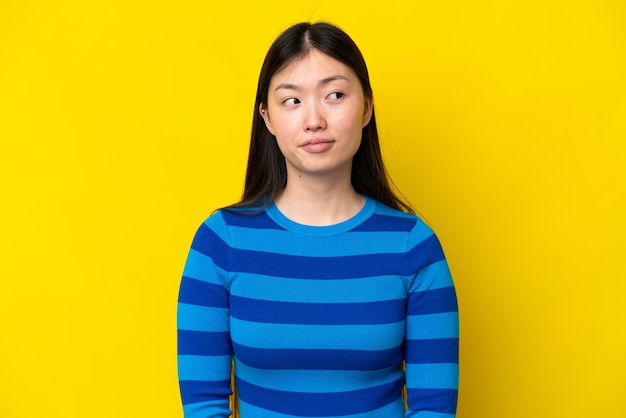 Young Chinese woman isolated on yellow background making doubts gesture looking side