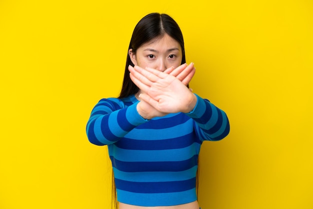 Young Chinese woman isolated on yellow background making stop gesture with her hand to stop an act