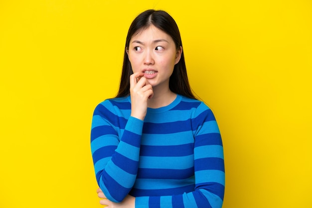 Young chinese woman isolated on yellow background nervous and scared