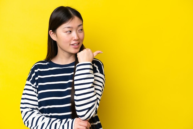 Young Chinese woman isolated on yellow background pointing to the side to present a product