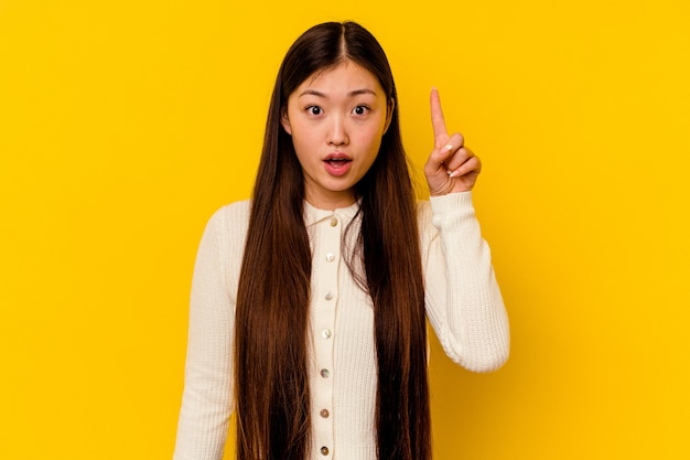 Young chinese woman isolated on yellow background pointing upside with opened mouth.