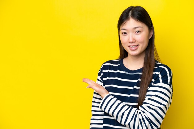 Young chinese woman isolated on yellow background presenting an idea while looking smiling towards