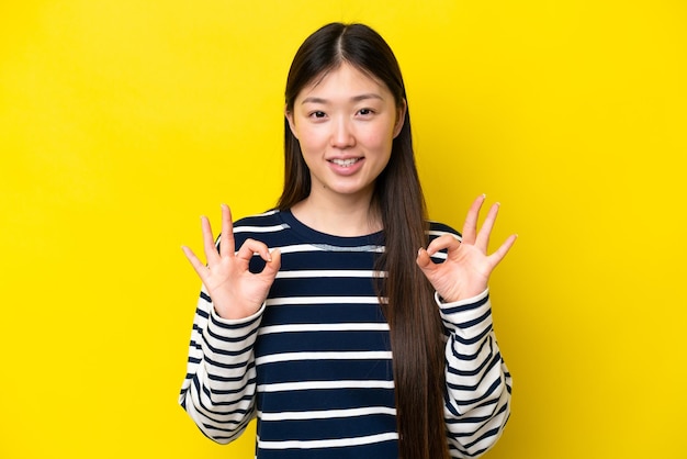 Young chinese woman isolated on yellow background showing ok sign with two hands