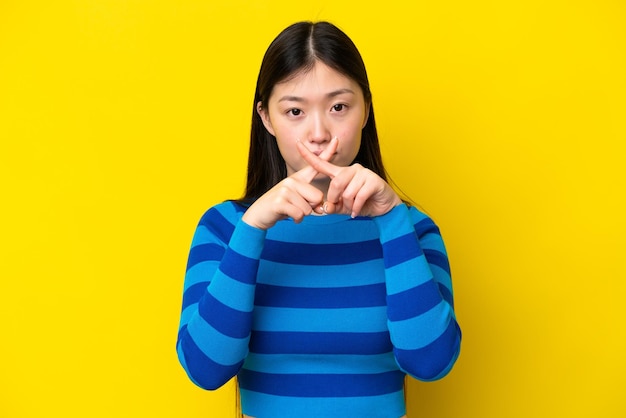 Young Chinese woman isolated on yellow background showing a sign of silence gesture