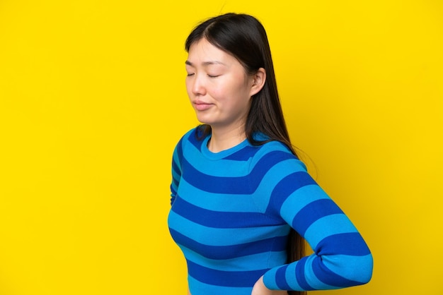 Young Chinese woman isolated on yellow background suffering from backache for having made an effort