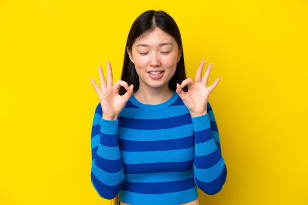 Young chinese woman isolated on yellow background in zen pose