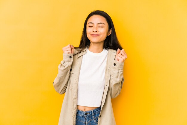 Young chinese woman isolated on a yellow wall raising fist, feeling happy and successful. Victory concept.