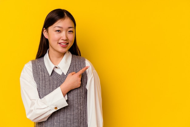 Young chinese woman isolated on yellow wall smiling and pointing aside, showing something at blank space.