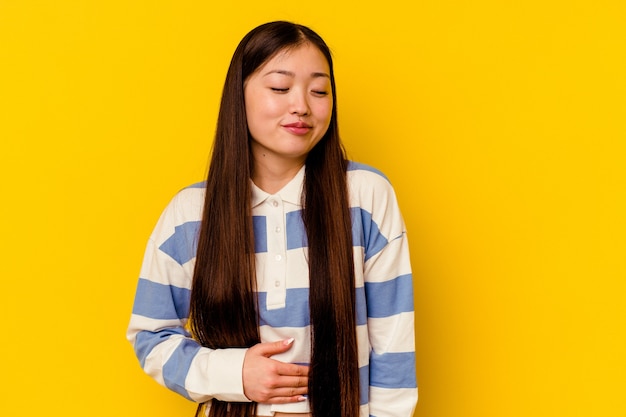 Молодая китаянка, изолированная на желтой стене, трогает животик, нежно улыбается, ест и удовлетворяет концепции.