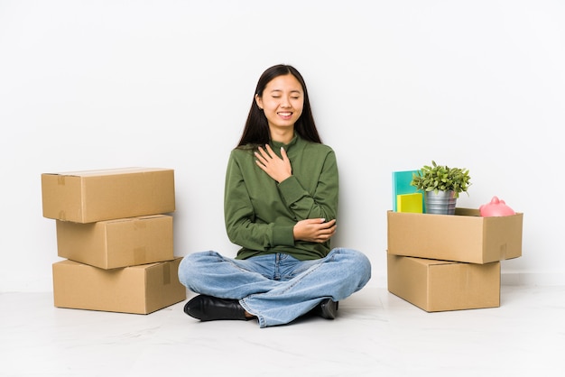 Young chinese woman moving to a new home laughs happily and has fun keeping hands on stomach.