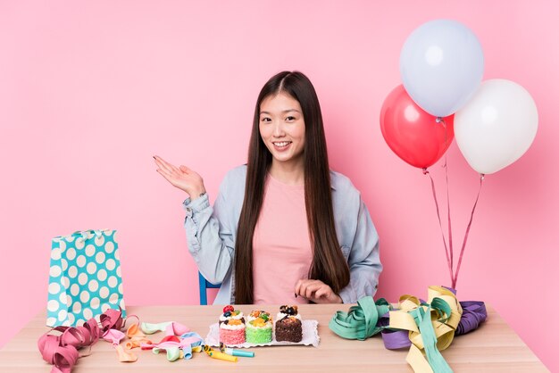Young chinese woman organizing a birthday isolated showing a copy space on a palm and holding another hand on waist.