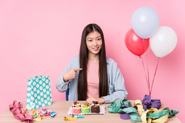 Young chinese woman organizing a birthday person pointing by hand to a shirt blank space