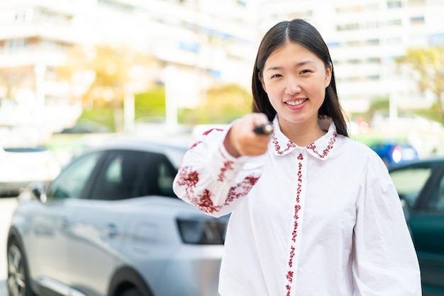 幸せそうな表情で車のキーを保持している屋外で若い中国人女性