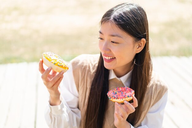 幸せな表情でドーナツを保持している屋外で若い中国人女性