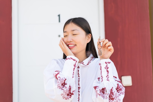 Young Chinese woman at outdoors holding home keys with happy expression