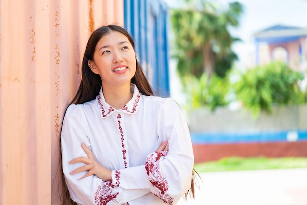 Young Chinese woman at outdoors looking up while smiling