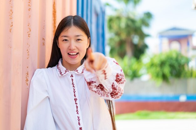 Young Chinese woman at outdoors surprised and pointing front