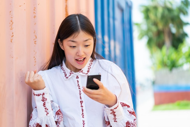 屋外で驚いてメッセージを送信する若い中国人女性