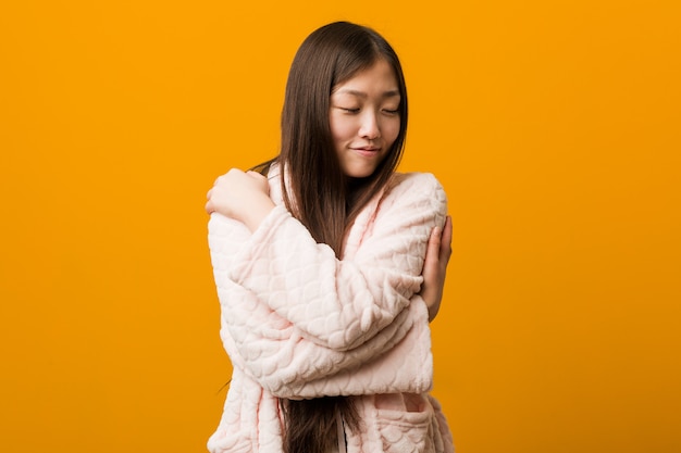 Young chinese woman in pajama hugs himself, smiling carefree and happy.