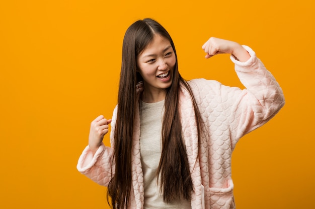 Young chinese woman in pajama raising fist after a victory, winner concept