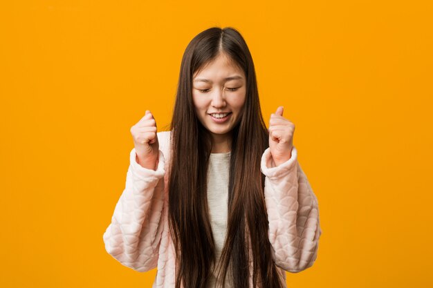 젊은 중국 여자 파자마 주먹을 올리는 행복하고 성공적인 느낌. 승리.