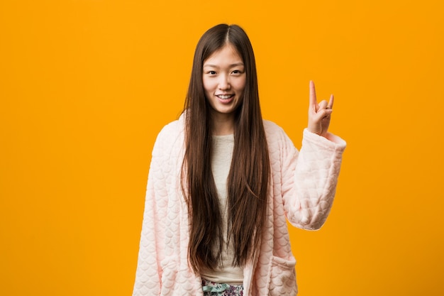 Young chinese woman in pajama showing a horns gesture as a revolution concept.