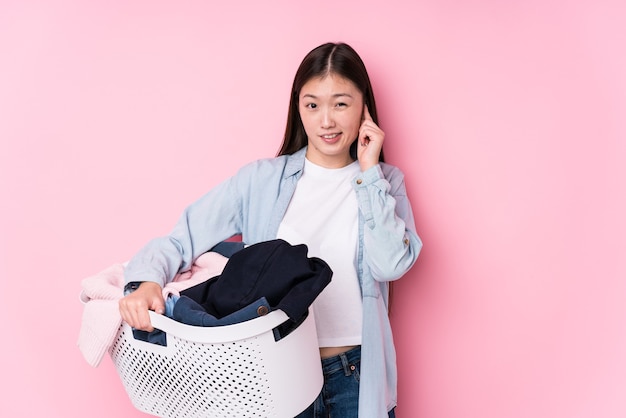 Young chinese woman picking up dirty clothes isolated covering ears with hands.