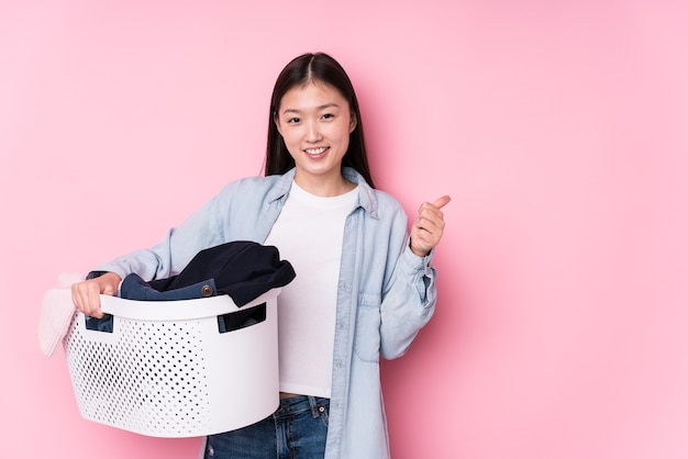 Young chinese woman picking up dirty clothes isolated smiling and raising thumb up