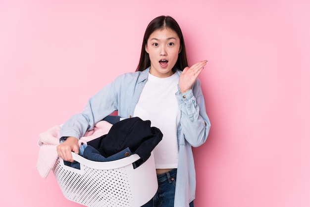 Young chinese woman picking up dirty clothes isolated surprised and shocked.