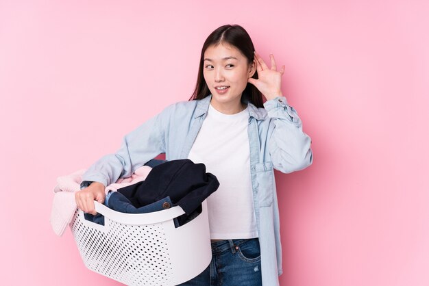 Young chinese woman picking up dirty clothes trying to listening a gossip.