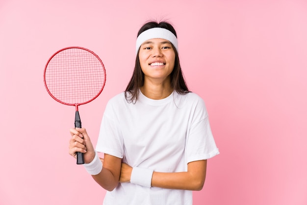 Young chinese woman playing badminton in a pink wall laughing and having fun.