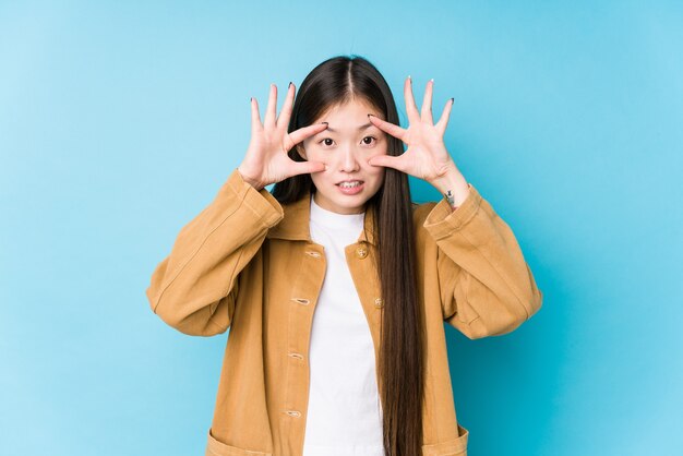 Young chinese woman posing in a blue surface isolated keeping eyes opened to find a success opportunity.