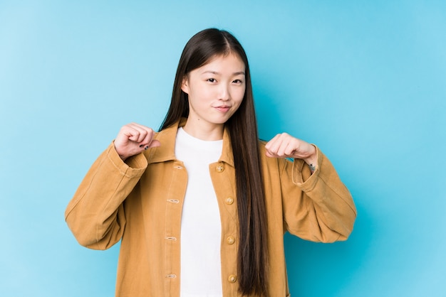 Young chinese woman posing in a blue wall feels proud and self confident, example to follow.