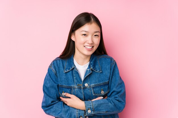 Young chinese woman posing in a pink background isolated laughing and having fun.