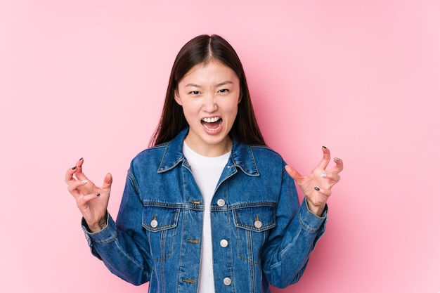 Young chinese woman posing on pink isolated screaming with rage.