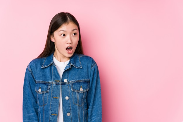 Young chinese woman posing in a pink wall isolated being shocked because of something she has seen.