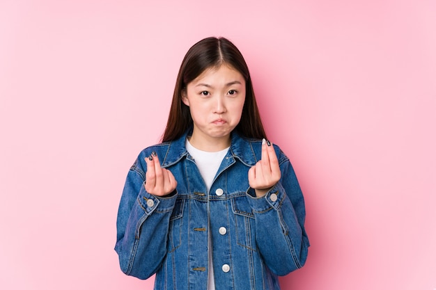 Young chinese woman posing in a pink wall showing that she has no money.